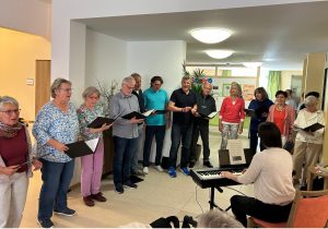 Ein Foto vom Auftritt im Seniorenzentrum. Der Chor Cantiamo steht im Halbkreis vor seiner Chorleiterin, die den Chor sitzend am Klavier begleitet.